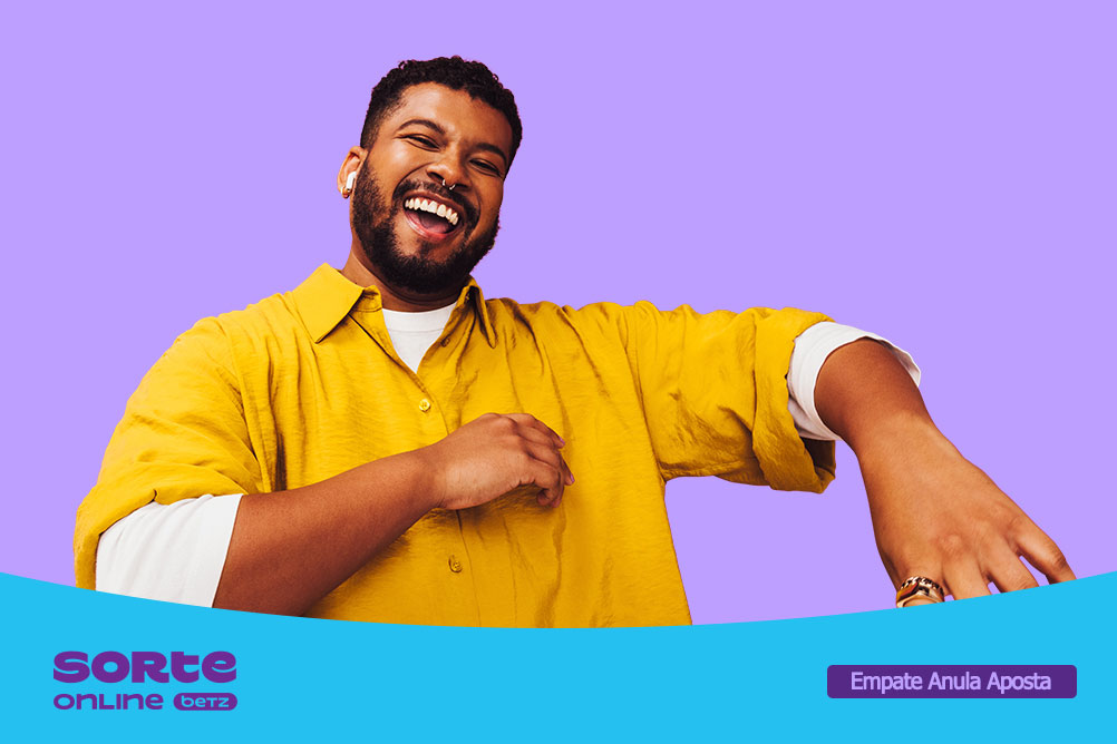 Homem sorridente vestindo uma camisa amarela sobre uma camiseta branca, em pose descontraída diante de um fundo lilás. Na parte inferior da imagem aparece a marca Sorte Online Betz e o destaque promocional “Empate Anula Aposta”.